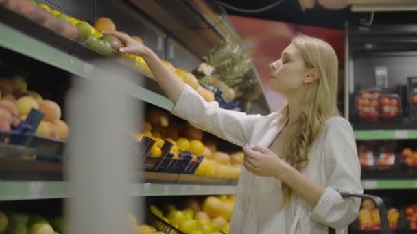 Молодая женщина выбирает спелые манго в продуктовом магазине. Веганы покупают фрукты и овощи в органическом супермаркете и используют многоразовые пакеты. 4K Slow . — стоковое видео