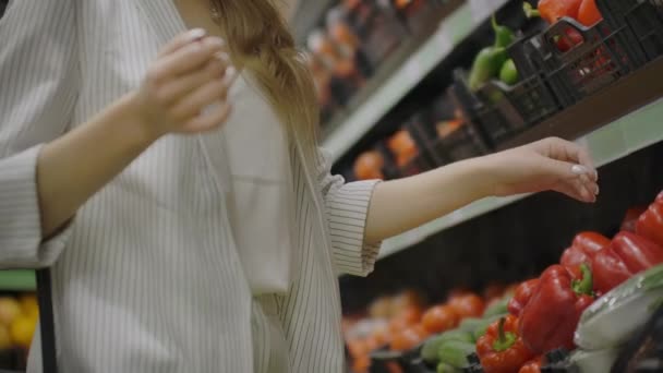 スーパーマーケットで赤唐辛子を買う女性。食料品店で有機野菜を選ぶ女性の手。ゼロ廃棄物ショッピングと健康的なライフスタイルコンセプト。スローモーション. — ストック動画