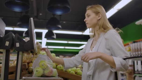 Mujer de mediana edad pesa una bolsa de manzanas en el supermercado . — Vídeos de Stock