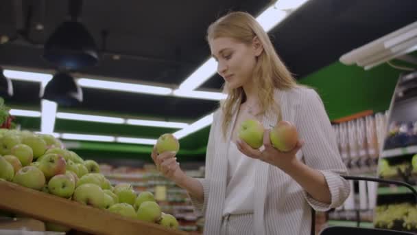 Atractiva joven mujer eligiendo manzana en supermercado de frutas y verduras . — Vídeo de stock