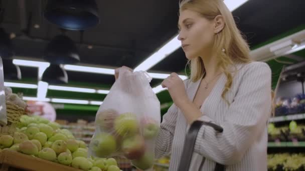 Mujer de mediana edad pesa una bolsa de manzanas en el supermercado . — Vídeos de Stock