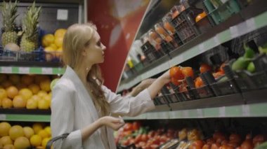 Kız, ev hanımı süpermarkette alışveriş. Bir dal üzerinde taze domates seçer, bir selofan çanta, kravat onları koyar. Onları bir arabaya koyar