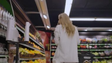 Meyve rafları dikkate elinde bir sepet ile süpermarkette yürüyen geri kız görünümü.