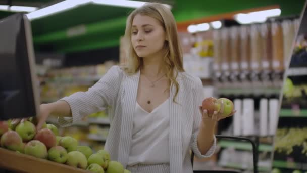 Attraktive junge Frau wählt Apfel am Obst- und Gemüsemarkt. — Stockvideo