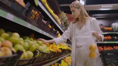 Süpermarkette güzel bir sarışın portakal seçer ve terazi tartmak için bir çanta onları koyar