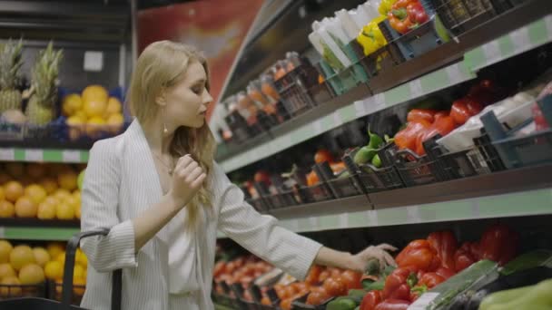 Девушка, домохозяйка, покупающая в супермаркете. Выбирает свежие помидоры на ветке, кладет их в целлофановый мешок, галстуки. Их и кладет в тележку. — стоковое видео