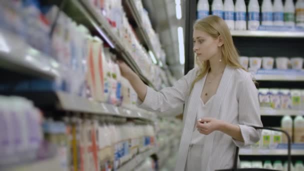 Anunciar, Negocios, Alimentos, Concepto de Salud - Mujer en un supermercado de pie frente al congelador y elegir la compra de botella de leche fresca. Beber leche para una alimentación saludable — Vídeos de Stock