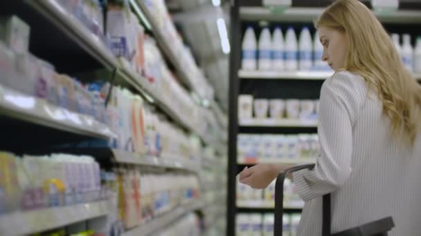 Egy nő sétál a hűtőszekrényben, és kiválaszt egy üveg tejet, felveszi és beolvassa a címkét