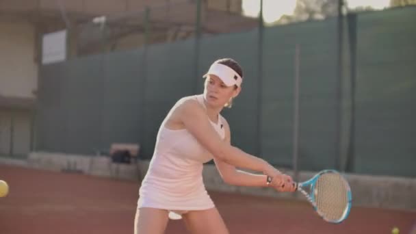 Жінка тенісистка на тенісному корті грає в теніс у повільному русі з ракеткою і на заході сонця — стокове відео