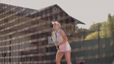 Beyaz dar takım elbiseli profesyonel bir kadın raketle topa vurur ve tenis kortunda dinamik olarak oynar.