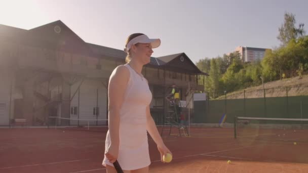 Junges hübsches Mädchen spielt Tennis. Eine Frau im weißen Trainingsanzug trainiert professionell Tennis. junges hübsches Mädchen spielt Tennis. Tennisangebot — Stockvideo