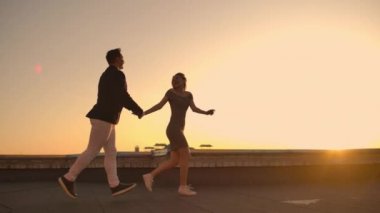 Şehrin arka planında gün batımında binanın çatısında koşan ve kenarında duran sevimli aşıklar gülüyor. Romantizm ve aşk.