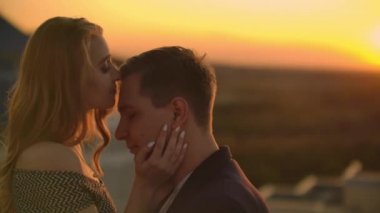 Lovely tatlı happines çift şehir şehir üzerinde inanılmaz günbatımı manzarası ile çatı üstünde oturup. Birbirlerini seviyorlar çok şefkat güneş saç arasında gider kucaklar.