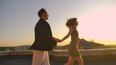 Şehrin arka planında gün batımında binanın çatısında koşan ve kenarında duran sevimli aşıklar gülüyor. Romantizm ve aşk.