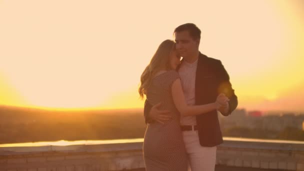 Two lovers embracing dancing on top of a skyscraper overlooking the city at sunrise sunset. Romantic setting. — Stock Video