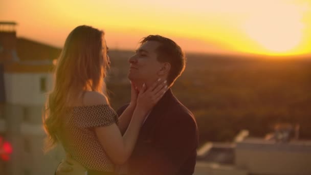 Encantador casal feliz doce sentar-se no topo do telhado com incrível vista para o pôr do sol na cidade urbana da cidade. Eles amam uns aos outros abraços muito ternura sol vai entre o cabelo . — Vídeo de Stock