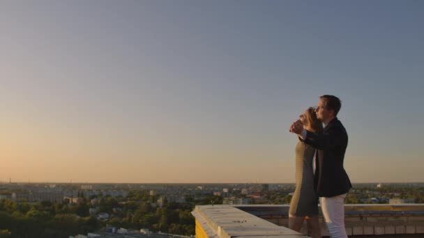 Na střeše se nachází nádherný, sladký, krásný pár, s úžasným výhledem na západ slunce v městském městě. Navzájem se milují, že slunce velmi něžně přechází mezi vlasy. — Stock video