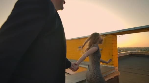 Young couple holding hands walking woman leading boyfriend the roof of the building at sunset POV travel concept. Carefree free lovers run on the roof laughing and smiling. — Stock Video