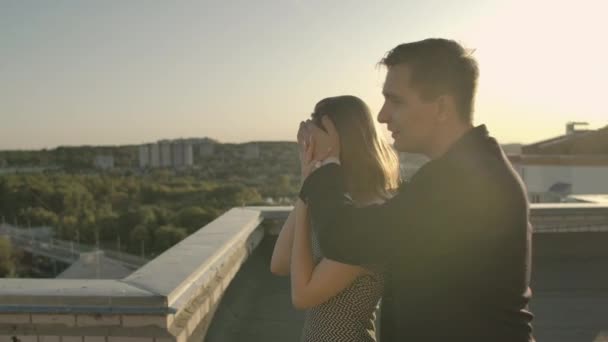 Дата на даху, чоловік веде дівчину закриваючи очі, готуючи романтичний сюрприз. Показувати прекрасний вид на захід сонця. Жінка насолоджується сюрпризом і посміхається, дивлячись на красиву — стокове відео
