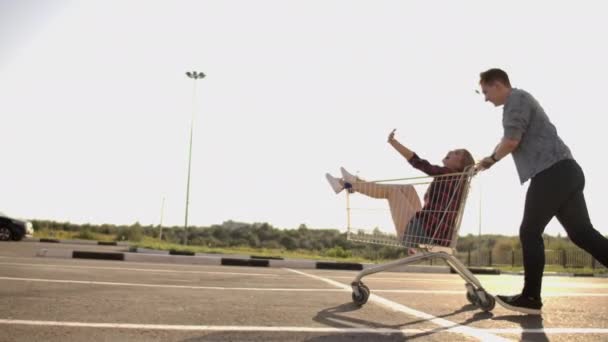 Mladí přátelé se baví na nákupních trollejích. Multietnické mladé lidi závodí na nákupním vozíku. Zpomaleně. — Stock video