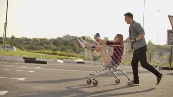 Young friends having fun on shopping trolleys. Multiethnic young people racing on shopping cart. slow motion. — Stock Video