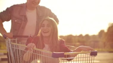 Açık havada park yerinde alışveriş arabasıyla gezen çift. Genç şık coupe süpermarket yakınındaki açık otoparkta alışveriş sepeti ile sürme eğlenceli.