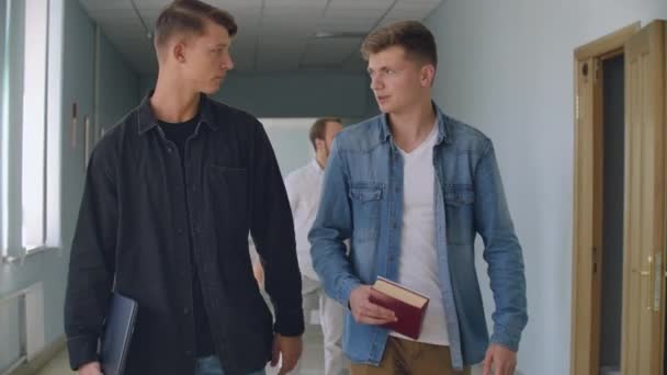 Een groep studenten lopen langs de gang van de Universiteit, school, College, communiceren, praten en glimlach. Een grote groep mensen lopen in de hal van een onderwijsinstelling met boeken — Stockvideo