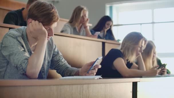 Grupo multi étnico de estudantes usando smartphones durante a palestra. Jovens usando as mídias sociais enquanto estudam na Universidade . — Vídeo de Stock