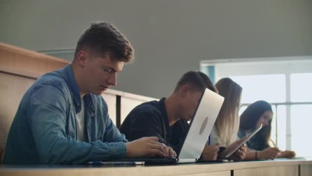 Grand groupe d'étudiants multi-ethniques travaillant sur les ordinateurs portables tout en écoutant une conférence dans la salle de classe moderne. Des jeunes brillants étudient à l'université 
