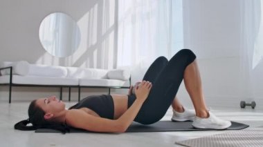 Spor giyimli kadın kalça köprüsü egzersizi yapıyor. Neşeli çekici genç kadın oturma odasında yerde yatan ve kalça köprü egzersiz yapıyor.