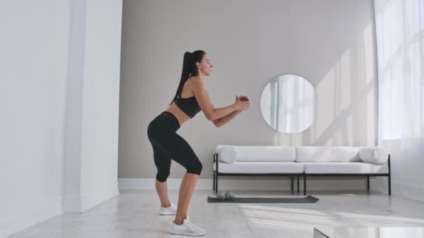 Menina ajuste bonito fazendo treino em casa realizando lunges laterais em uma sala de estar . — Vídeo de Stock