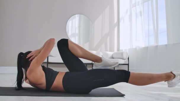 Chica joven haciendo ejercicios de crunches de bicicleta, haciendo ejercicio en casa. Chica de fitness joven haciendo ejercicios de bicicleta intensivos fáciles en casa tumbado en el suelo, deportivo . — Vídeos de Stock