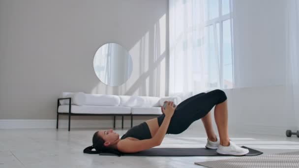 Mujer en ropa deportiva haciendo ejercicio de puente de cadera. Joven atractiva alegre tumbada en el suelo en la sala de estar y haciendo ejercicio de puente de cadera . — Vídeos de Stock