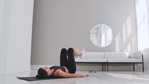Entrenamiento de fuerza entrenamiento de peso corporal mujer atleta haciendo patadas aleteo. Europea mujer adulta haciendo ejercicios de suelo con la pierna se levanta para ejercitar los músculos abdominales en casa en su apartamento . — Vídeos de Stock