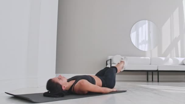 Entrenamiento de deportista en casa. Ajuste atleta femenina haciendo ejercicio de un solo brazo con el dedo del pie tumbado en el piso en apartamento blanco — Vídeo de stock