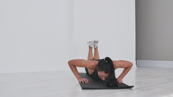 Ung sexig brunett kvinna i sportkläder utför armhävningar knäböjer hemma på en matta. — Stockvideo