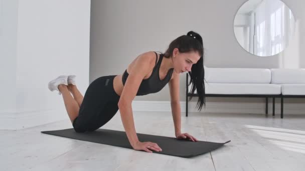 Jeune femme brune sexy en vêtements de sport effectue des pompes à genoux à la maison sur un tapis . — Video