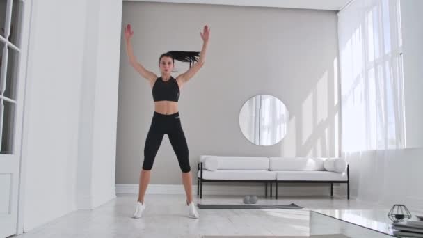 Vrouw doet Jumping Jacks thuis. Sportswoman doen Jumping Jacks oefening thuis. — Stockvideo
