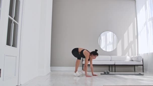 Fitness-Frau beim Burpee-Workout zu Hause. mittlere Aufnahme einer jungen Frau, die Liegestütze macht und in Zeitlupe springt. Sportkonzept. — Stockvideo