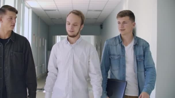 Três estudantes do sexo masculino caminham pelo corredor e conversam — Vídeo de Stock