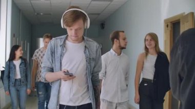 Bir adam Kolej'in koridorunda yürürken müzik dinler ve akıllı telefonun ekranına bakar.