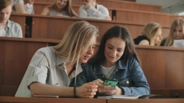 Güzel kız öğrenciler smartphone, ekran, söz ve oturma masaları üniversitede gülerek izliyor kullanıyorsunuz. Sosyal medya, internet, millennials ve eğitim kavramı.