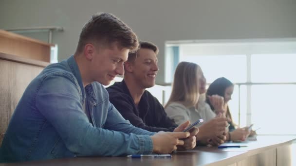 Deux amis sont assis dans une grande salle de classe avec des élèves et se montrant des vidéos drôles du pensionnat .