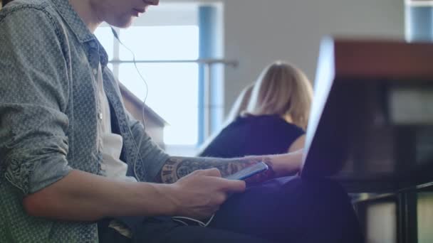 Un étudiant dans un auditorium de l'Université écoute de la musique dans des écouteurs blancs pendant une pause sans prêter attention aux autres. Beaucoup de gens dans le public parlent 
