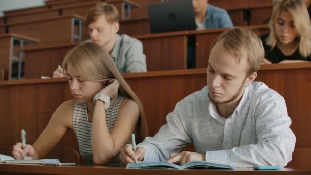 O público atual da faculdade em que os alunos ouvem o professor e escrevem um relatório de curta-metragem no caderno. Transferir conhecimento e educar os alunos — Vídeo de Stock