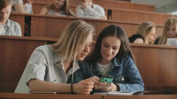 Mooie meisjes studenten gebruiken smartphone, scherm, kijken, praten en lachen vergadering om bureaus aan de Universiteit. Sociale media, internet, millennials en onderwijs concept. — Stockvideo