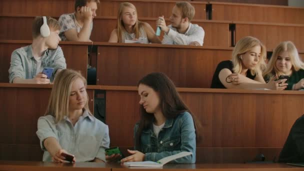 Mooie meisjes studenten gebruiken smartphone, scherm, kijken, praten en lachen vergadering om bureaus aan de Universiteit. Sociale media, internet, millennials en onderwijs concept. — Stockvideo