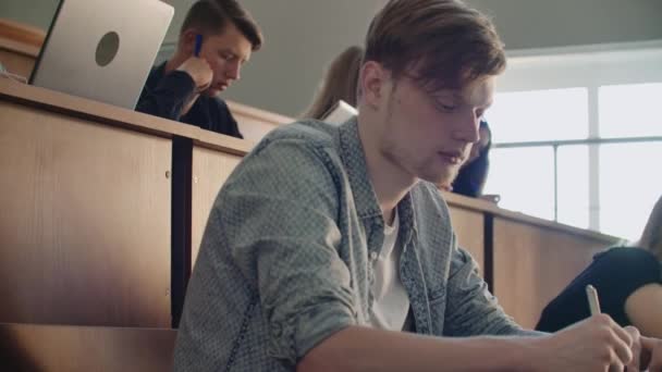 Kameran rör sig genom publiken där studenterna skriver en föreläsning på bärbara datorer och anteckningsböcker för professorer i ett stort klassrum av ett universitet eller högskola — Stockvideo