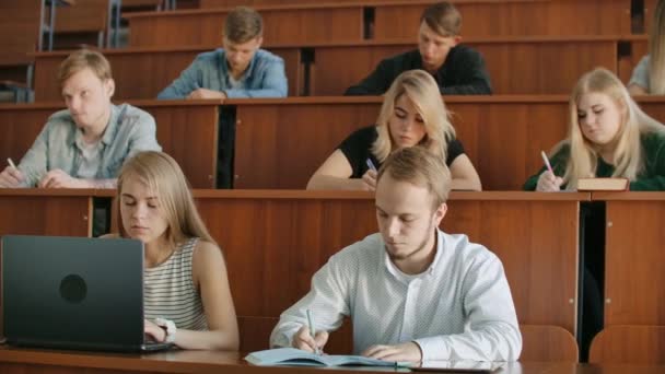 Un gruppo di studenti tra il pubblico ascolta l'insegnante e scrive un riassunto della lezione — Video Stock