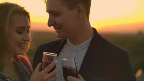 Um jovem casal no telhado bebendo vinho de óculos de pé em um cobertor e admirando o belo pôr do sol sobre a cidade. Noite romântica no telhado com vista para a cidade . — Vídeo de Stock